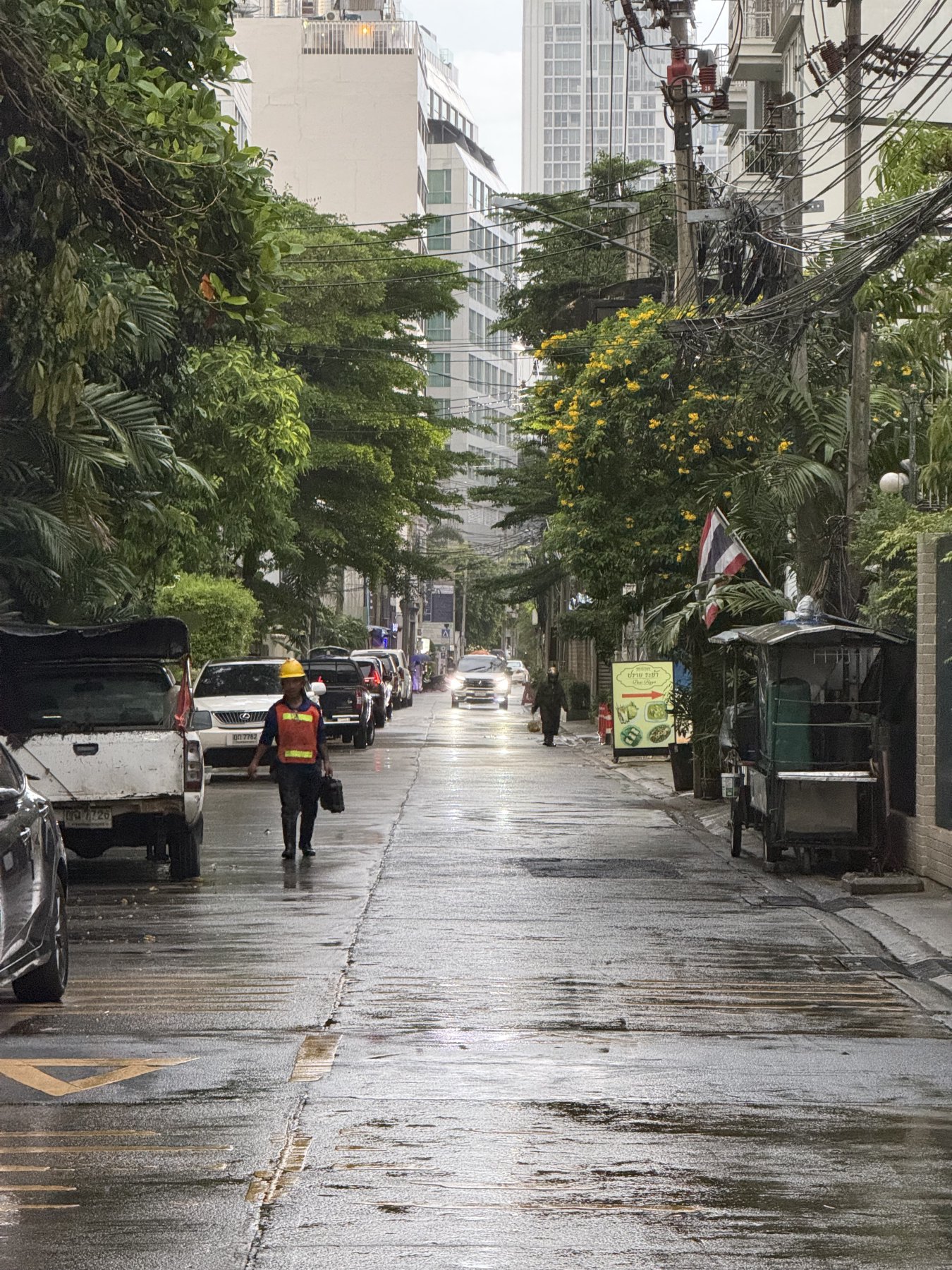 Evening north looking view of rainy street with man walking and oncoming car in distance. On Sukhumvit 8 in downtown.