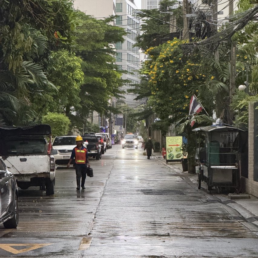 Evening north looking view of rainy street with man walking and oncoming car in distance. On Sukhumvit 8 in downtown.